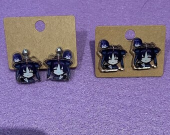 May include: Two pairs of earrings featuring a cartoon character with black hair and a purple hat. The earrings are on brown card stock.