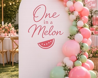May include: A white arched backdrop featuring the pink text One in a Melon and a watermelon slice graphic. A balloon garland in shades of pink, white, and sage green with small white flowers cascades down the right side of the arch.