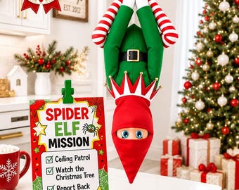May include: A plush elf doll hanging upside down by a red and white striped rope, wearing a green tunic with a black belt and a red pointed hat. Beside it, a sign reads Spider Elf Mission with checkboxes for Ceiling Patrol, Watch the Christmas Tree, and Report Back to Santa.