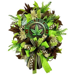 Pode incluir: Uma coroa verde, marrom e branca com uma placa que diz "Bem-vindo ao nosso Joint". A placa tem uma folha de maconha verde.