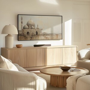 May include: A living room with a light wood cabinet, a white sofa, a coffee table, and a lamp. A flat screen TV is mounted on the wall above the cabinet. The TV is displaying a painting of a mosque.