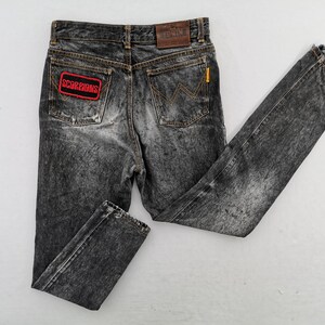May include: Acid-washed black denim jeans featuring a rectangular red and black Scorpions patch on the left back pocket, a brown leather Edwin brand label on the waistband, and a signature W-stitch design on the right back pocket.