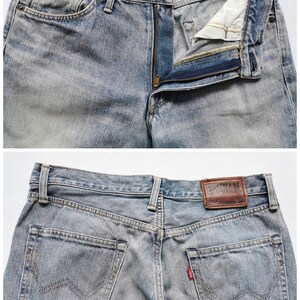 May include: Faded light blue denim jeans with a button and zip fly. The jeans feature front and back pockets, belt loops, and a brown leather brand patch. A small red tag is visible on the back pocket.