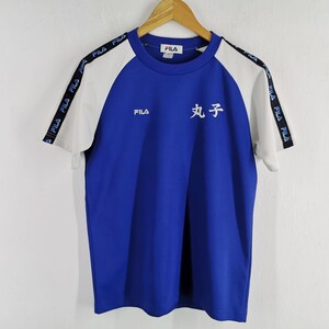 Puede incluir: Camiseta Fila azul y blanca de manga corta. La camiseta tiene mangas blancas y cuerpo azul. El logo de Fila est&aacute; en el pecho y las mangas tienen el logo de Fila impreso. Caracteres japoneses impresos en la parte delantera.