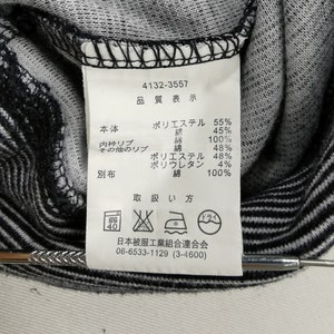 May include: Close-up of a clothing tag with Japanese text and symbols. The tag lists fabric composition percentages, including polyester and cotton. Washing instructions are also displayed. The garment has a black and white striped pattern.
