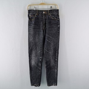 May include: High-waisted jeans in a faded black acid wash finish. These denim pants feature a classic five-pocket design, a metal button closure at the waist, a zip fly, and copper-toned rivets. The fabric displays a mottled, worn-in texture.