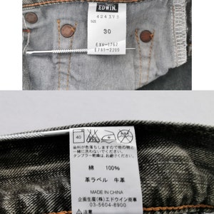 May include: Close-up of the inside of a pair of gray denim jeans. The jeans have a tag with the brand "EDWIN" and the size "30". The tag also includes care instructions and material information.