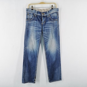 May include: Blue denim jeans with a faded wash effect, hanging on a gold-colored hanger. The jeans have a classic five-pocket design, a button and zipper closure, and a decorative pattern on the waistband.