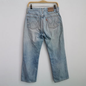 以下が含まれることがあります： 色あせたウォッシュ加工のライトブルーデニムジーンズ。Edwinブランドのラベルと赤いタグが付いています。ジーンズは、クラシックな5ポケットデザインとストレートレッグカットです。ジーンズは木製のハンガーに吊るされています。