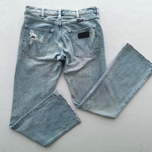 Pu&ograve; includere: Jeans in denim blu chiaro con dettagli strappati sulle tasche posteriori e sulle ginocchia. Presenta un classico design a cinque tasche, passanti per cintura e una toppa in pelle nera con il logo del marchio.