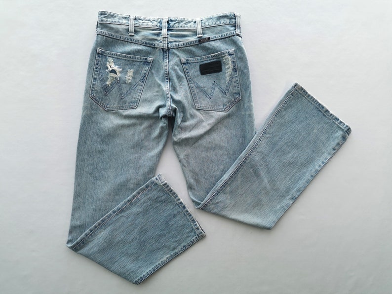 Pu&ograve; includere: Jeans in denim blu chiaro con dettagli strappati sulle tasche posteriori e sulle ginocchia. Presenta un classico design a cinque tasche, passanti per cintura e una toppa in pelle nera con il logo del marchio.
