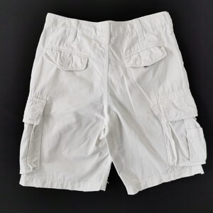 May include: White cargo shorts with multiple pockets, including two side pockets and two back pockets. The shorts have a button and zip closure and belt loops. The shorts are made of a durable fabric.