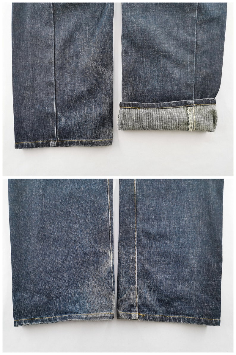 May include: Detailed view of dark wash denim jeans. The image displays the hems and cuffs of the jeans. One cuff is turned up, exposing the lighter inner fabric. The jeans feature yellow stitching and a classic straight-leg design.