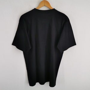 May include: A solid black t-shirt hanging on a wooden hanger against a white wall. The short-sleeved shirt is made of a soft material and has a crew neck. The shirt is a basic, everyday garment.