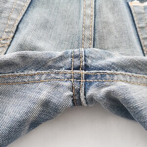 K&ouml;nnte beinhalten: Nahaufnahme einer hellblauen Jeans. Das Bild zeigt die Nahtdetails, mit sichtbaren N&auml;hten und einem kreuzgen&auml;hten Bereich. Der Denim hat ein abgenutztes Aussehen.