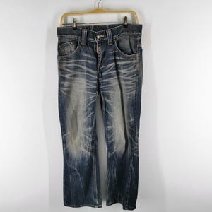 Op de afbeelding: Blauwe denim jeans met een vervaagd waseffect. De jeans hebben een klassiek ontwerp met vijf zakken, een knoop- en ritssluiting en hangen aan een houten hanger. De jeans hebben een rechte pijp.