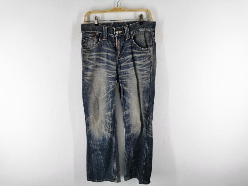 Op de afbeelding: Blauwe denim jeans met een vervaagd waseffect. De jeans hebben een klassiek ontwerp met vijf zakken, een knoop- en ritssluiting en hangen aan een houten hanger. De jeans hebben een rechte pijp.