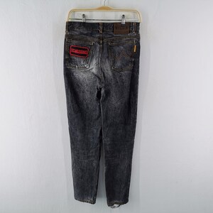 May include: Black acid-wash denim jeans featuring a rectangular red patch with the text SCORPIONS on the left back pocket, a brown leather brand label on the waistband, and a signature W-shaped stitching detail on the right back pocket.