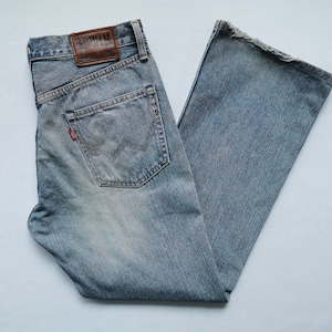 May include: Faded light blue denim jeans with a classic five-pocket design. Features a leather patch with the brand name "Edwin" and a red logo tag. The jeans have a straight leg and a worn appearance. The jeans are made of denim.