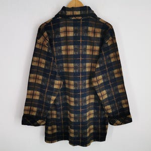 Puede incluir: Camisa de manga larga con botones y estampado de cuadros en tonos marr&oacute;n, azul marino y beige. La camisa tiene cuello y pu&ntilde;os abotonados. La parte trasera de la camisa es visible, colgada de una percha de madera.