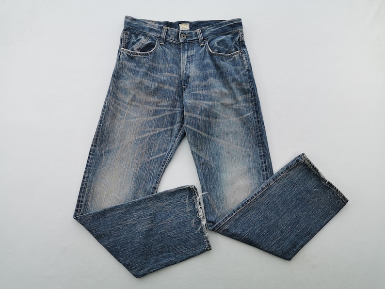 May include: Blue denim jeans with a faded wash and distressed details. The jeans have a classic five-pocket design, a button fly, and a straight leg. The denim is a medium wash with lighter fading.