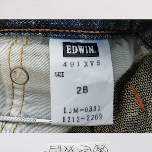 Op de afbeelding: Close-up van een blauwe denim jeans met zichtbare stiksels en een label. Het label luidt "EDWIN" en bevat maat informatie: "28". De jeans is gemaakt van 100% katoen en vervaardigd in Vietnam.