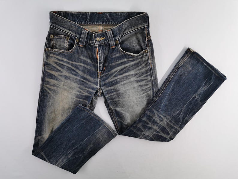 Op de afbeelding: Blauwe denim jeans met een vervaagde, versleten uitstraling. De jeans hebben een klassiek ontwerp met vijf zakken, een knoop- en ritssluiting en een licht uitlopende pijp. De stof vertoont slijtagepatronen.