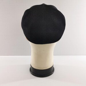 Puede incluir: Gorra negra con textura, tipo newsboy, exhibida en una cabeza de maniqu&iacute;. La gorra tiene una corona redondeada y una visera corta y r&iacute;gida. La tela parece ser un material tejido. La cabeza del maniqu&iacute; es blanquecina y la base es negra.