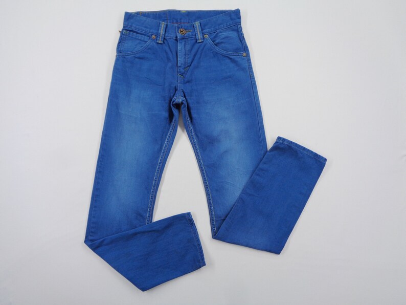 K&ouml;nnte beinhalten: Blaue Jeans aus Denim mit klassischem F&uuml;nf-Taschen-Design. Die Jeans haben einen Knopf- und Rei&szlig;verschluss, G&uuml;rtelschlaufen und Kontrastn&auml;hte. Das Kleidungsst&uuml;ck liegt flach auf einer wei&szlig;en Oberfl&auml;che.