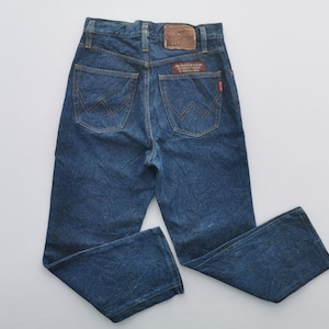 Puede incluir: Vaqueros de mezclilla azules con un dise&ntilde;o cl&aacute;sico de cinco bolsillos. Los vaqueros tienen un parche de cuero marr&oacute;n y una etiqueta roja en el bolsillo trasero. El logotipo de Wrangler es visible en los bolsillos traseros. Los vaqueros son de lavado medio.