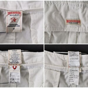 May include: Detail of the waistband and labels of white True Religion jeans. The labels show the brand logo, size 29, and manufacturing details. The fabric appears to be a cotton and polyester blend.