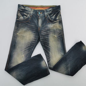 Pu&ograve; includere: Jeans di denim blu strappati con un lavaggio sbiadito e cuciture arancioni. I jeans hanno una chiusura con bottoni e un bottone turchese. I pantaloni in denim hanno un classico design a cinque tasche e una vestibilit&agrave; rilassata.