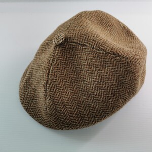 Op de afbeelding: Bruine tweed newsboy cap met een visgraatpatroon. De pet is gemaakt van een textuurstof en heeft een kleine, afgeronde klep. Een klassieke hoedstijl die geschikt is voor diverse gelegenheden.