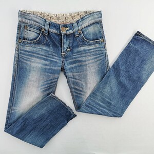 May include: Blue denim jeans with a faded wash and decorative stitching. The jeans feature a classic five-pocket design, a button and zipper closure, and a patterned waistband. The jeans are folded and laid flat, showcasing their details.