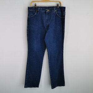 May include: Dark blue denim jeans hanging on a wooden hanger. The jeans have a classic five-pocket design, a button and zipper closure, and a straight leg fit. The jeans are made of a sturdy denim material and are suitable for everyday wear.
