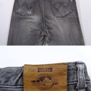 Puede incluir: Primer plano de unos vaqueros Edwin grises. Los vaqueros tienen un dise&ntilde;o cl&aacute;sico de cinco bolsillos con un parche de cuero en la cintura trasera. El parche dice "INTERNATIONAL BASIC" y "EDWIN CO. LTD.". Los vaqueros son de color gris descolorido.
