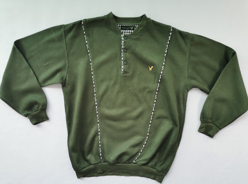 May include: An olive green long-sleeved sweatshirt with a button-up collar and a small embroidered logo. The collar and front panels are trimmed with white and black striped detail. The cuffs and hem are ribbed.