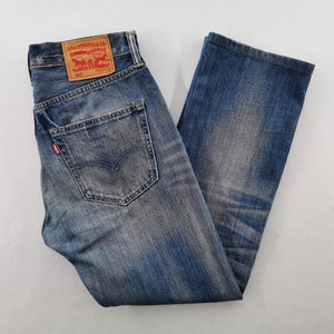May include: Blue denim jeans featuring a faded wash, a tan leather patch on the back waistband with the text Levi Strauss & Co. 505 31 32, a back pocket with a red tab, and a classic five-pocket construction with visible stitching and metal rivets.