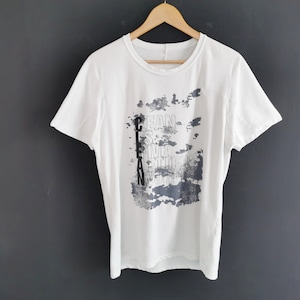 Puede incluir: Camiseta blanca con cuello redondo y mangas cortas, colgada de una percha de madera. La camiseta presenta un diseño gráfico gris y azul con las palabras "CLEAN IS THE NEW WORD".