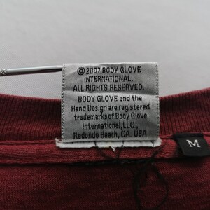 May include: A close-up of a burgundy t-shirt label with the text "&copy;2007 BODY GLOVE INTERNATIONAL. ALL RIGHTS RESERVED." The label also includes the Body Glove trademark and the location "Redondo Beach, CA. USA."