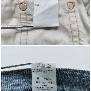 May include: Detailed view of the inside of blue denim jeans, featuring the "EDWIN" brand label and a size tag. The tags display care instructions and material details, including 100% cotton. The jeans have metal rivets and a light-colored interior.