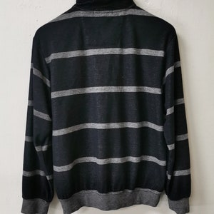 May include: Black and gray striped long-sleeve shirt with a mock neck collar. The shirt features horizontal gray stripes across the black fabric. The cuffs and hem are also gray.