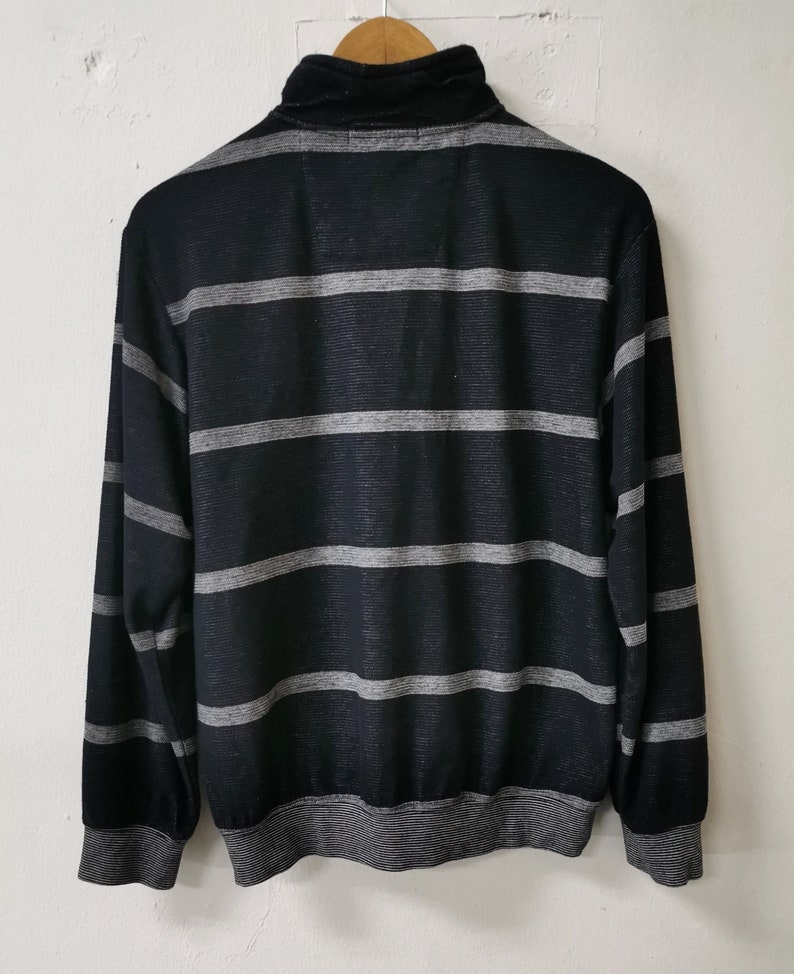 May include: Black and gray striped long-sleeve shirt with a mock neck collar. The shirt features horizontal gray stripes across the black fabric. The cuffs and hem are also gray.