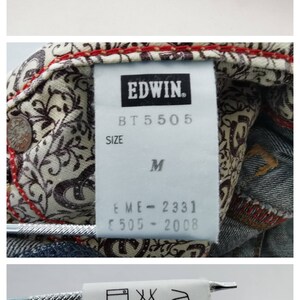 May include: Close-up of blue denim jeans with visible stitching and a detailed label. The label reads "EDWIN" and includes size information. The jeans have a medium wash and are likely vintage or a classic style.