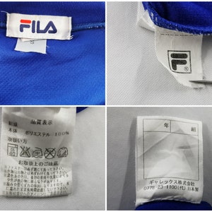 Puede incluir: Primer plano de una chaqueta deportiva azul con detalles blancos. El logotipo de FILA es visible en una etiqueta blanca. Etiquetas adicionales muestran instrucciones de cuidado y texto japon&eacute;s. La chaqueta est&aacute; hecha de 100% poli&eacute;ster.