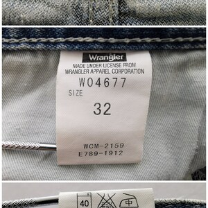 Pu&ograve; includere: Primo piano di jeans blu in denim con un'etichetta nera Wrangler. L'etichetta recita "GREENSBORO, N.C., U.S.A." &Egrave; visibile un'etichetta taglia 32. I jeans sono realizzati su licenza di Wrangler Apparel Corporation.