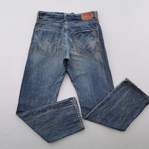 May include: Blue denim jeans with a faded wash and classic five-pocket design. The jeans have a straight leg cut and a leather patch on the back waistband. The denim has a worn look.