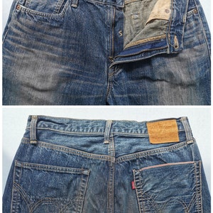 Pu&ograve; includere: Primo piano di jeans in denim blu con chiusura a bottone e cerniera. I jeans hanno tasche anteriori e posteriori, con una toppa in pelle marrone sul retro. Le tasche hanno accenti rossi. I jeans sono uno stile classico.
