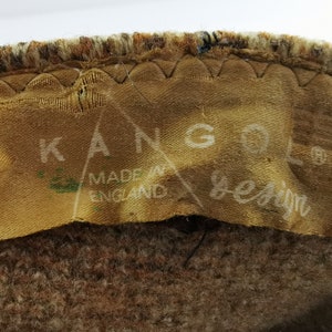 Op de afbeelding: Close-up van een bruine en tan stof met een label met de tekst "KANGOL design MADE IN ENGLAND". Het label is op de stof genaaid.