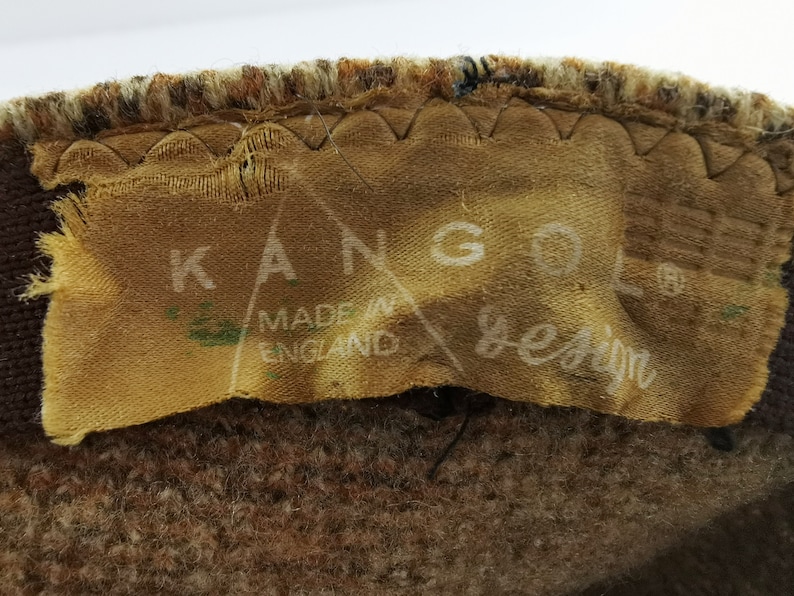 Op de afbeelding: Close-up van een bruine en tan stof met een label met de tekst "KANGOL design MADE IN ENGLAND". Het label is op de stof genaaid.
